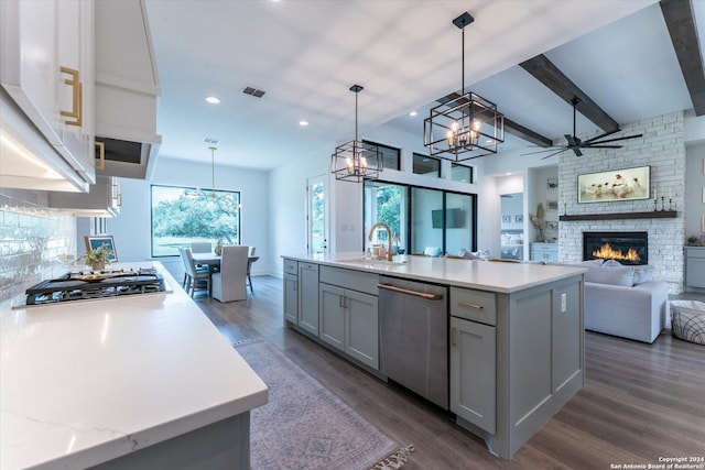 kitchen with stainless steel appliances, a center island with sink, decorative light fixtures, and dark hardwood / wood-style flooring