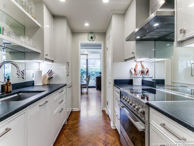 kitchen with dark parquet flooring, wall chimney range hood, white cabinets, high end stove, and sink