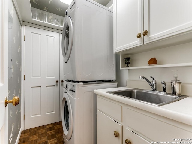 laundry area featuring stacked washer and clothes dryer, dark parquet floors, cabinets, and sink