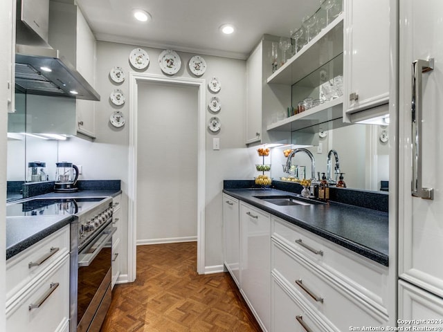 kitchen with stainless steel range, dark parquet floors, white cabinets, wall chimney range hood, and sink