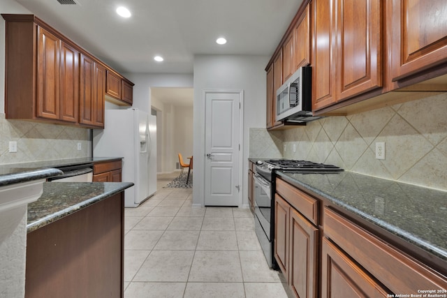 kitchen featuring stainless steel appliances, dark stone countertops, light tile patterned floors, and tasteful backsplash