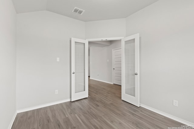 unfurnished bedroom with french doors, vaulted ceiling, and wood-type flooring