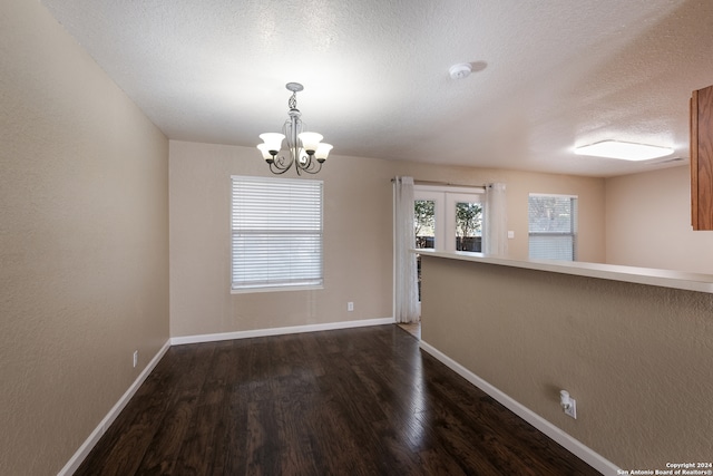 spare room featuring dark wood-type flooring, a textured ceiling, french doors, and a notable chandelier