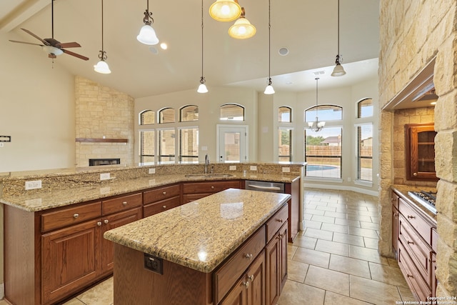 kitchen featuring high vaulted ceiling, a spacious island, a stone fireplace, sink, and hanging light fixtures