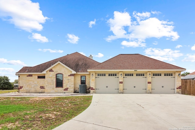 view of front of home with a garage, a front yard, and central AC