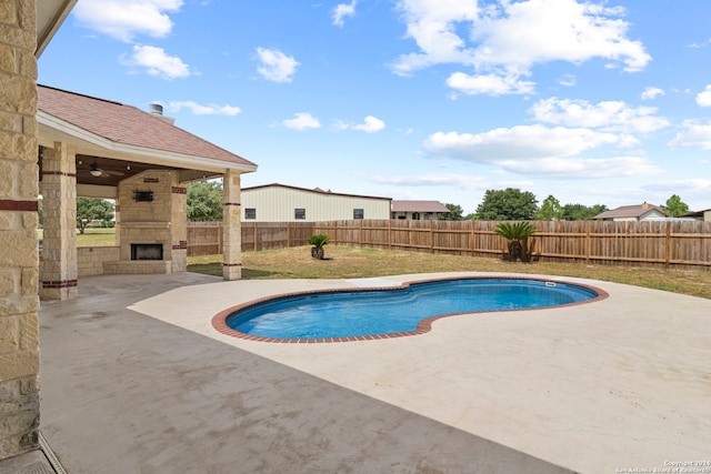 view of pool featuring an outdoor stone fireplace, a patio, and ceiling fan