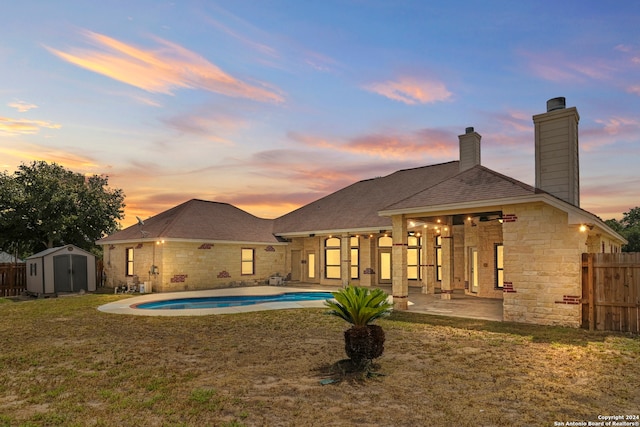 back house at dusk featuring a fenced in pool, a yard, a patio, and a storage shed