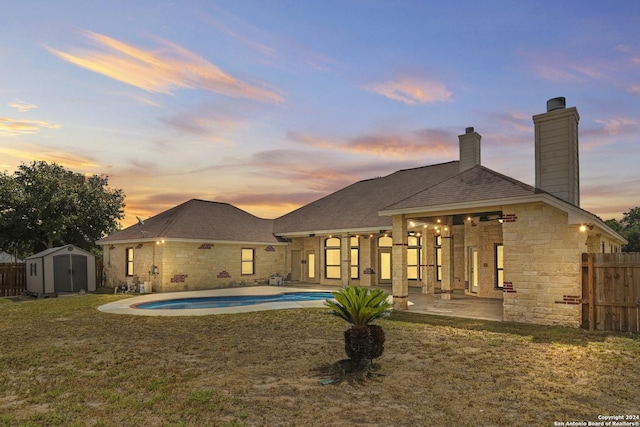 back house at dusk featuring a patio area, a fenced in pool, a yard, and a storage shed