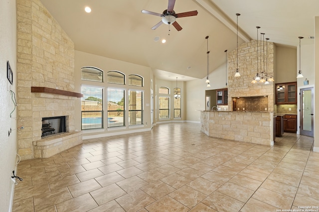 unfurnished living room with beam ceiling, a stone fireplace, high vaulted ceiling, light tile patterned floors, and ceiling fan with notable chandelier