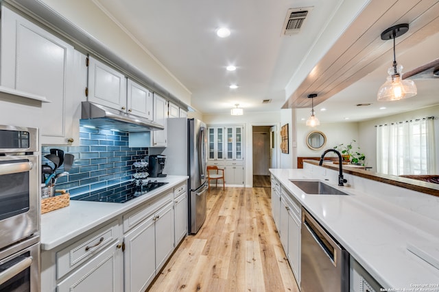 kitchen with crown molding, appliances with stainless steel finishes, decorative light fixtures, sink, and light hardwood / wood-style floors