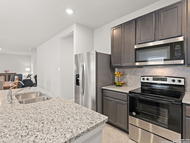 kitchen featuring light stone counters, sink, backsplash, dark brown cabinets, and appliances with stainless steel finishes