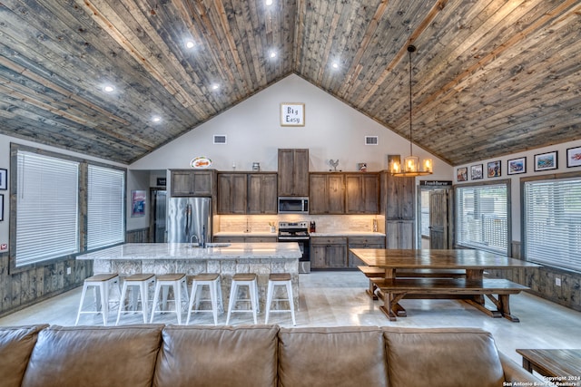 kitchen with a breakfast bar, high vaulted ceiling, pendant lighting, stainless steel appliances, and a kitchen island with sink