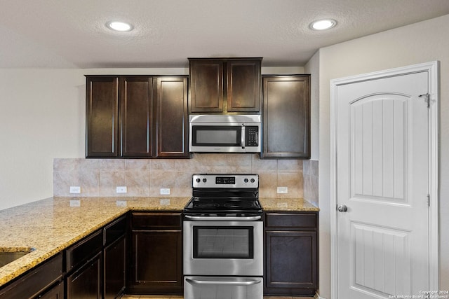 kitchen featuring backsplash, light stone countertops, appliances with stainless steel finishes, and dark brown cabinetry