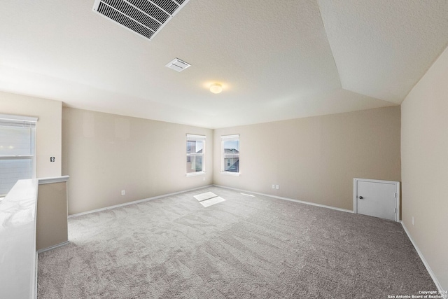 carpeted spare room featuring a textured ceiling and vaulted ceiling