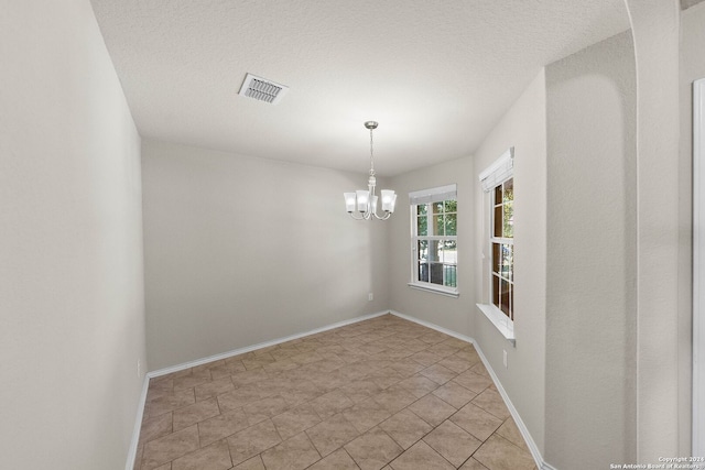 spare room featuring a textured ceiling, a notable chandelier, and light tile patterned floors