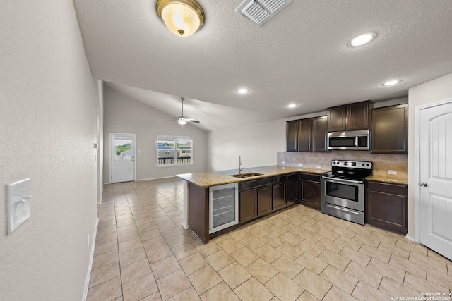 kitchen with kitchen peninsula, appliances with stainless steel finishes, dark brown cabinets, beverage cooler, and vaulted ceiling