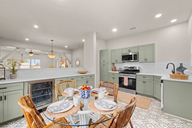 kitchen featuring appliances with stainless steel finishes, ceiling fan, green cabinetry, hanging light fixtures, and beverage cooler