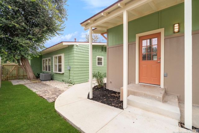 view of exterior entry featuring central AC and a yard