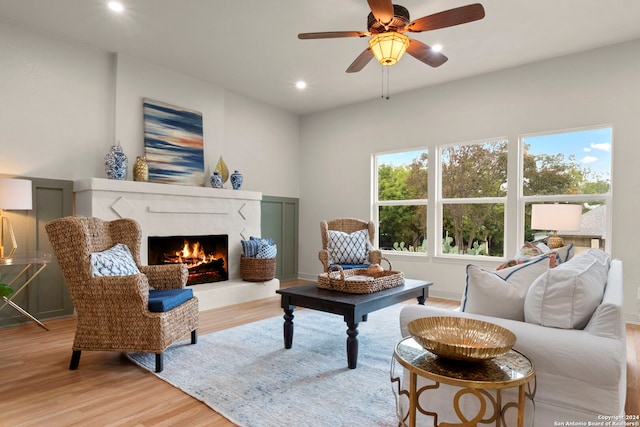 living room featuring a premium fireplace, light hardwood / wood-style flooring, and ceiling fan