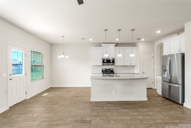 kitchen with white cabinetry, appliances with stainless steel finishes, pendant lighting, light stone countertops, and an island with sink