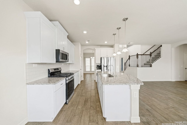 kitchen with white cabinets, light hardwood / wood-style flooring, an island with sink, pendant lighting, and appliances with stainless steel finishes