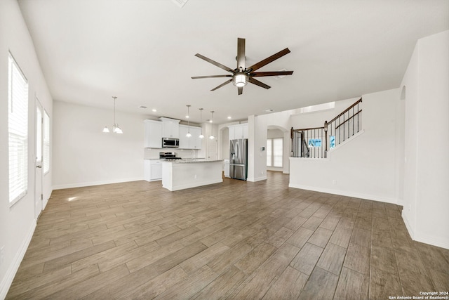 unfurnished living room with light hardwood / wood-style floors and ceiling fan with notable chandelier