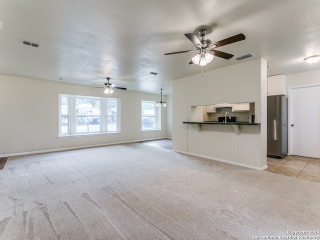 unfurnished living room with a textured ceiling, light colored carpet, and ceiling fan with notable chandelier