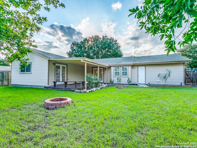 rear view of property featuring an outdoor fire pit and a lawn