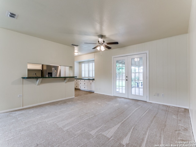 unfurnished living room featuring ceiling fan, light colored carpet, and french doors