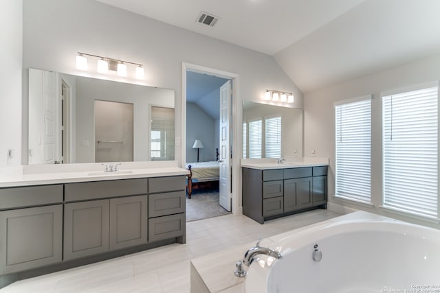 bathroom featuring vanity, tiled bath, and vaulted ceiling