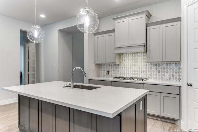 kitchen with stainless steel gas cooktop, a center island with sink, gray cabinets, and sink