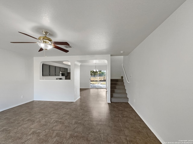 unfurnished living room with ceiling fan with notable chandelier and a textured ceiling