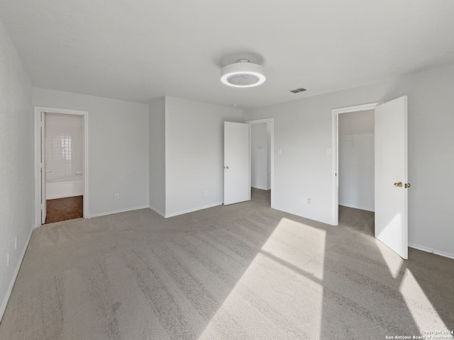 unfurnished bedroom featuring ensuite bath, carpet flooring, a closet, and a spacious closet