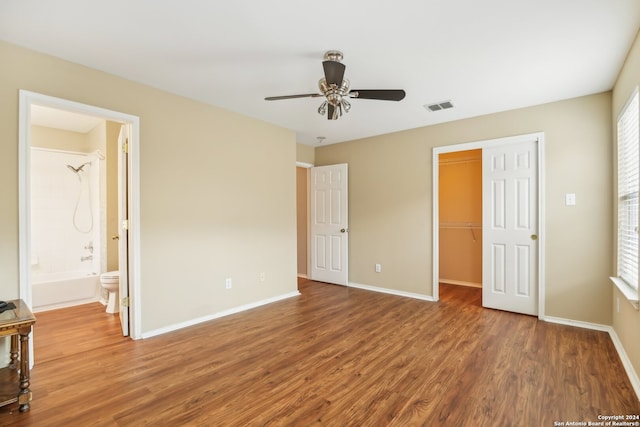 unfurnished bedroom with hardwood / wood-style floors, ceiling fan, ensuite bath, and a walk in closet