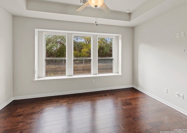 spare room with ceiling fan, a tray ceiling, a healthy amount of sunlight, and dark hardwood / wood-style floors