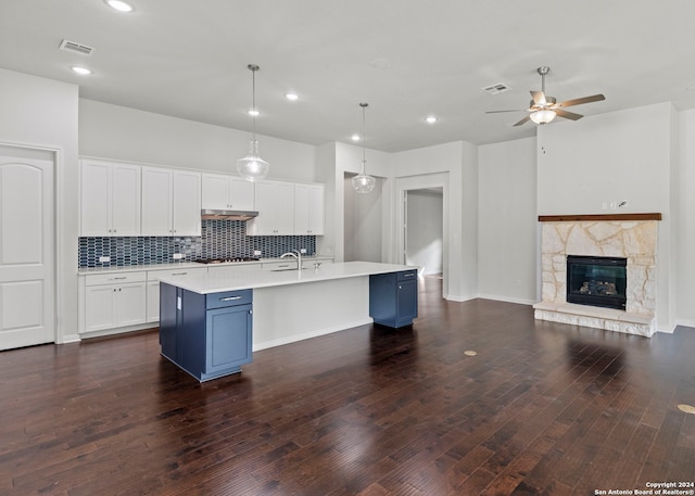 kitchen featuring a fireplace, white cabinetry, decorative light fixtures, dark hardwood / wood-style flooring, and a kitchen island with sink