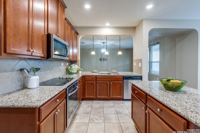 kitchen with light stone counters, stainless steel appliances, decorative light fixtures, sink, and kitchen peninsula