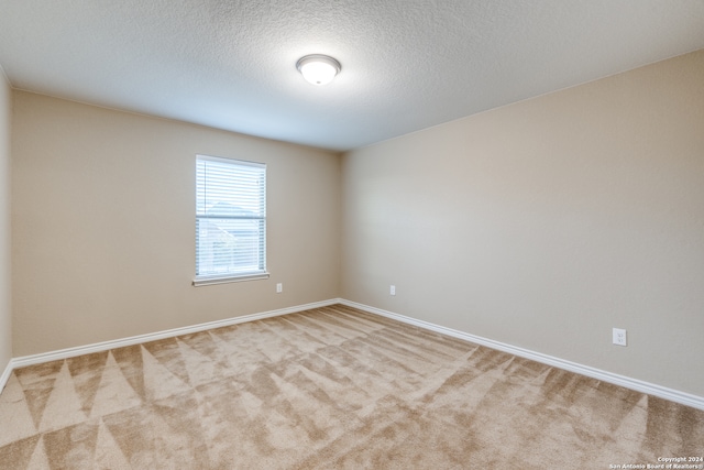 empty room with light colored carpet and a textured ceiling