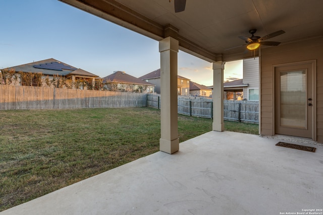 patio terrace at dusk featuring a lawn and ceiling fan