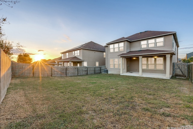 back house at dusk with a lawn and a patio