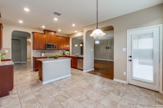 kitchen with pendant lighting, stainless steel appliances, backsplash, and light stone countertops