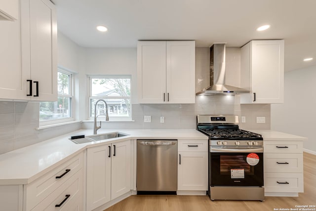 kitchen featuring stainless steel appliances, wall chimney exhaust hood, white cabinets, and light wood-type flooring