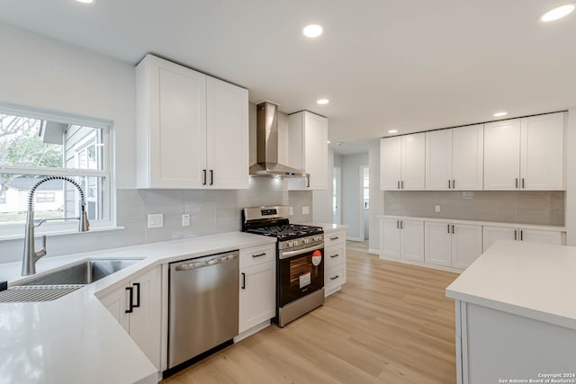 kitchen featuring light wood-type flooring, appliances with stainless steel finishes, sink, white cabinets, and wall chimney exhaust hood