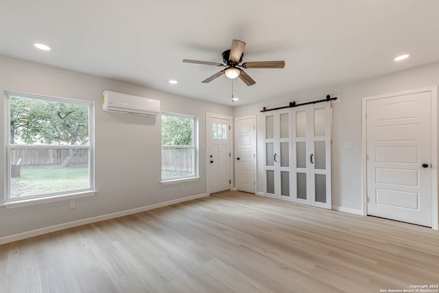 empty room featuring a wall mounted AC, plenty of natural light, a barn door, and light hardwood / wood-style flooring