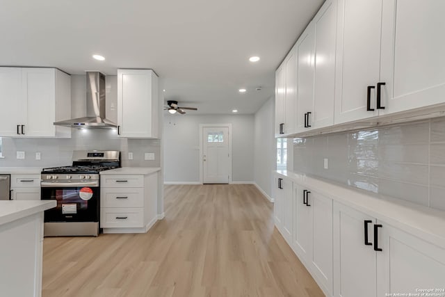 kitchen with stainless steel appliances, light wood-type flooring, wall chimney range hood, decorative backsplash, and white cabinets