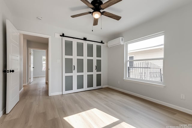 spare room featuring light hardwood / wood-style flooring, a barn door, an AC wall unit, and ceiling fan