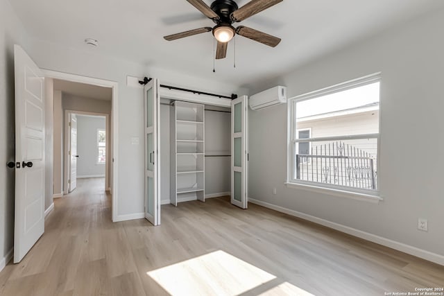 unfurnished bedroom featuring a closet, light wood-type flooring, a barn door, a wall mounted air conditioner, and ceiling fan