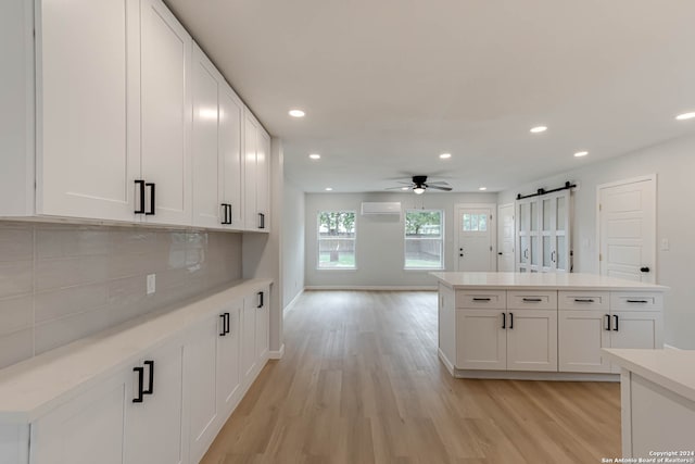 kitchen with light hardwood / wood-style floors, tasteful backsplash, a wall mounted AC, white cabinets, and a barn door