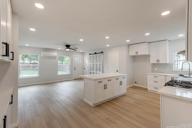 kitchen with white cabinetry, a barn door, a wall mounted air conditioner, ceiling fan, and light hardwood / wood-style flooring