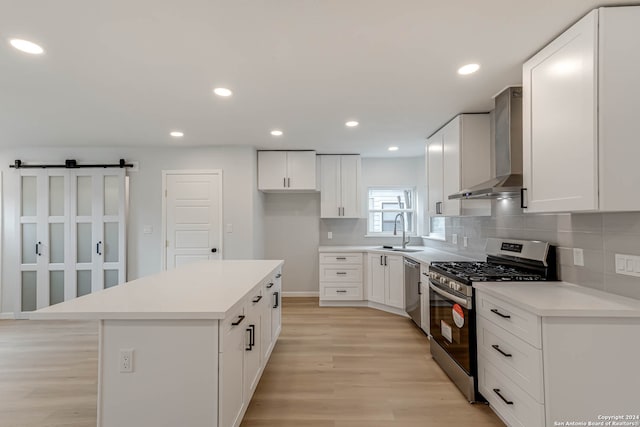 kitchen featuring light hardwood / wood-style floors, wall chimney exhaust hood, sink, a kitchen island, and appliances with stainless steel finishes